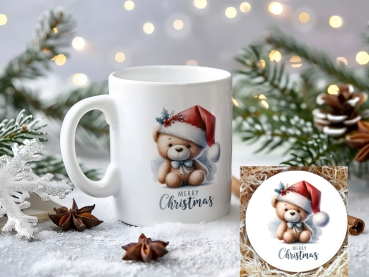 Weihnachtstasse mit niedlichem Bärchen in Weihnachtsmütze und Engelsflügeln, verziert mit dem Schriftzug 'Merry Christmas'. Perfektes Geschenk für die Weihnachtszeit, mit festlicher Dekoration im Hintergrund.